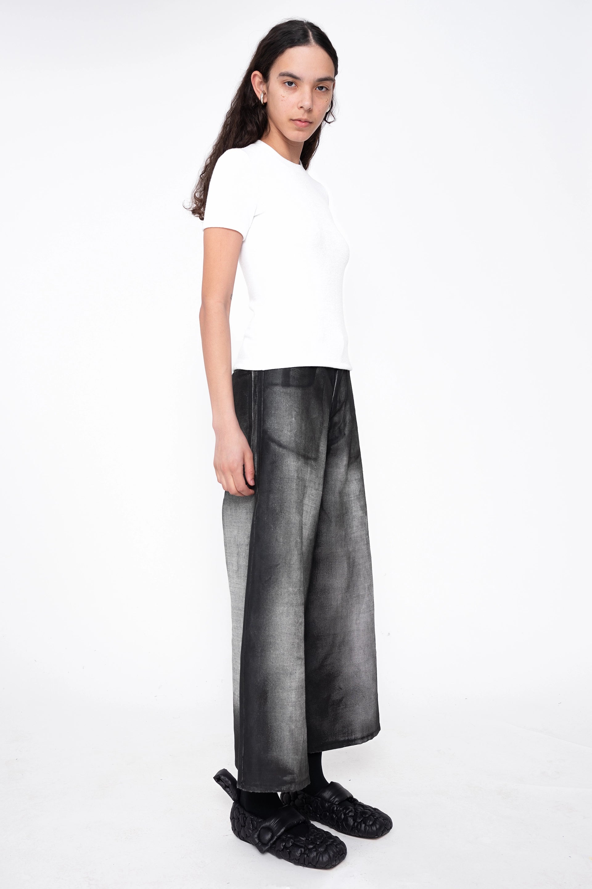 female-wearing-white-tee-and-cropped-grey-denim-pants-with-black-spray-paint-on-white-background-full-body-three-quarter