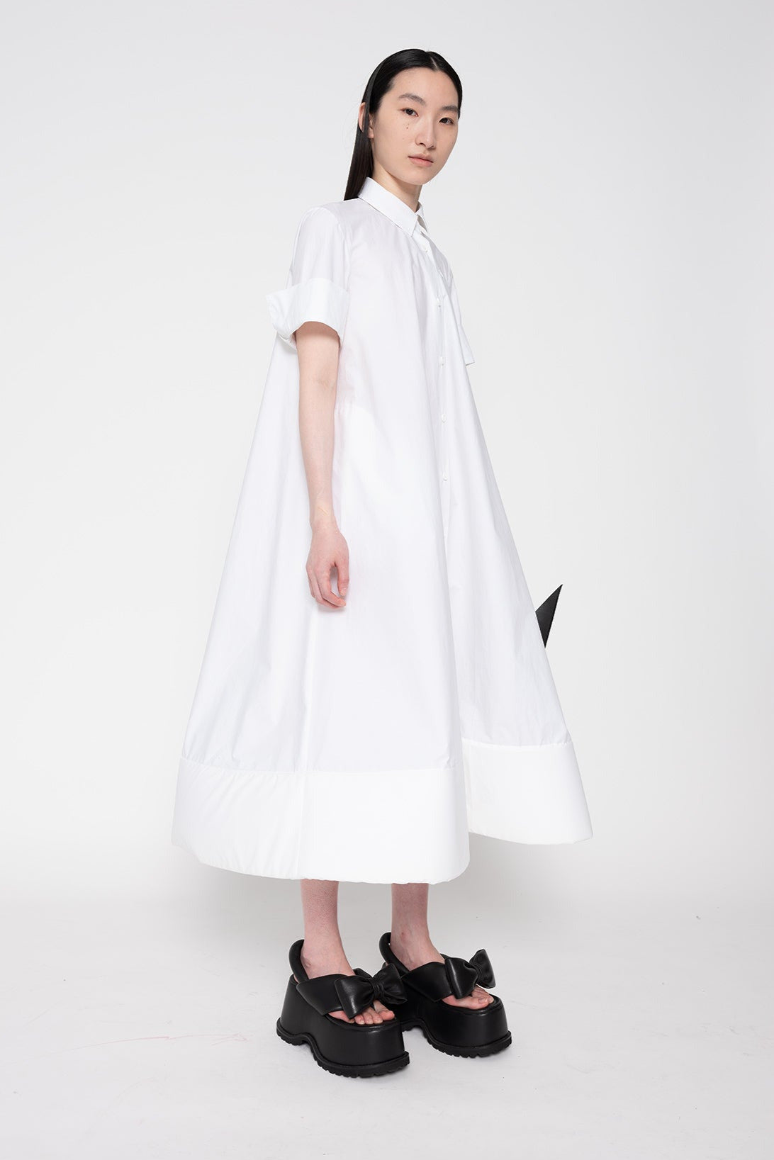 THREE-QUARTERS-VIEW-BRUNETTE-WOMAN-white-a-line-shaped-cotton-dress-with-foam-hem-detail-WEARING-BOW-PLATFORM-SANDALS-IN-BLACK