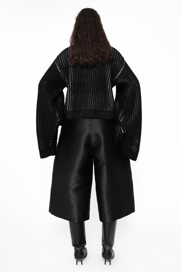 female-wearing-chunky-rib-knit-sweater-and-shiny-wide-leg-ulottes-with-double-heel-boots-on-white-background-full-body-back