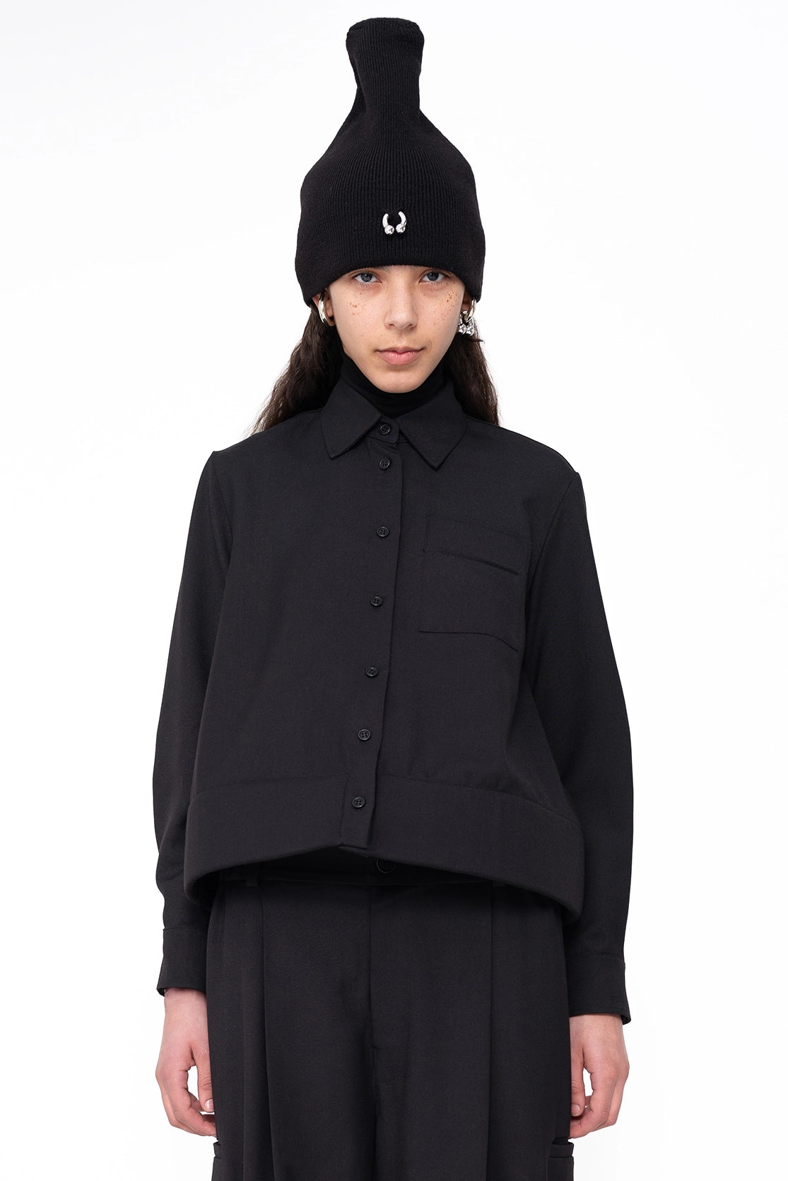 female-wearing-black-shirt-with-foam-hem-and-black-hat-with-piercing-detail-on-white-background-closeup-front