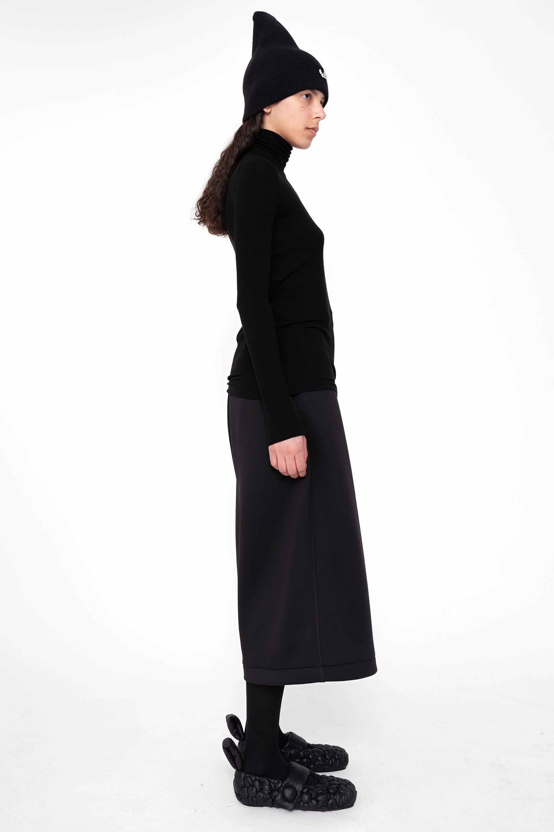 female-wearing-black-turtleneck-and-pierced-beanie-withwide-leg-culottes-on-white-background-full-body-side