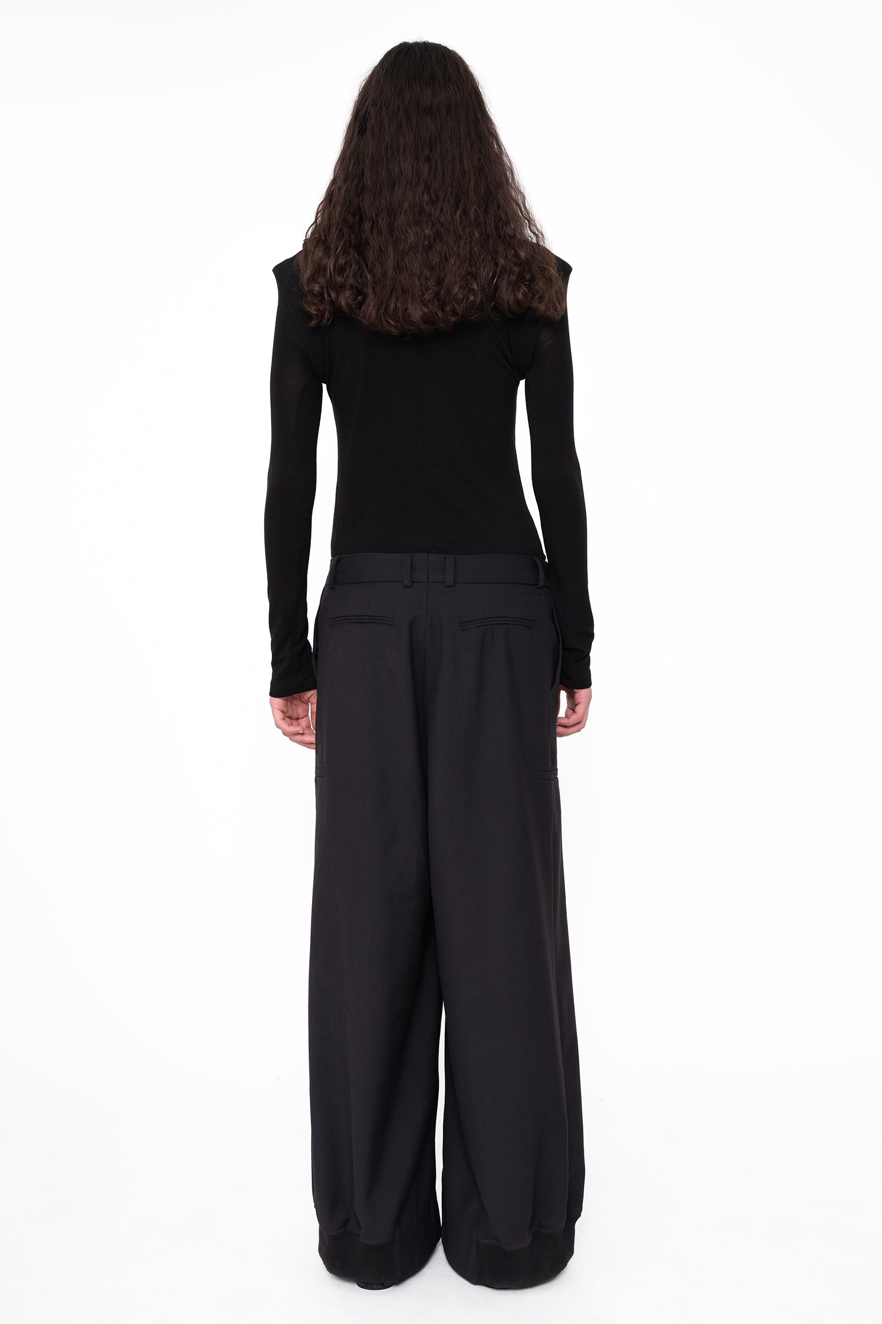 female-wearing-black-tight-turtleneck-with-tailored-wide-leg-suit-pants-on-white-background-full-body-back