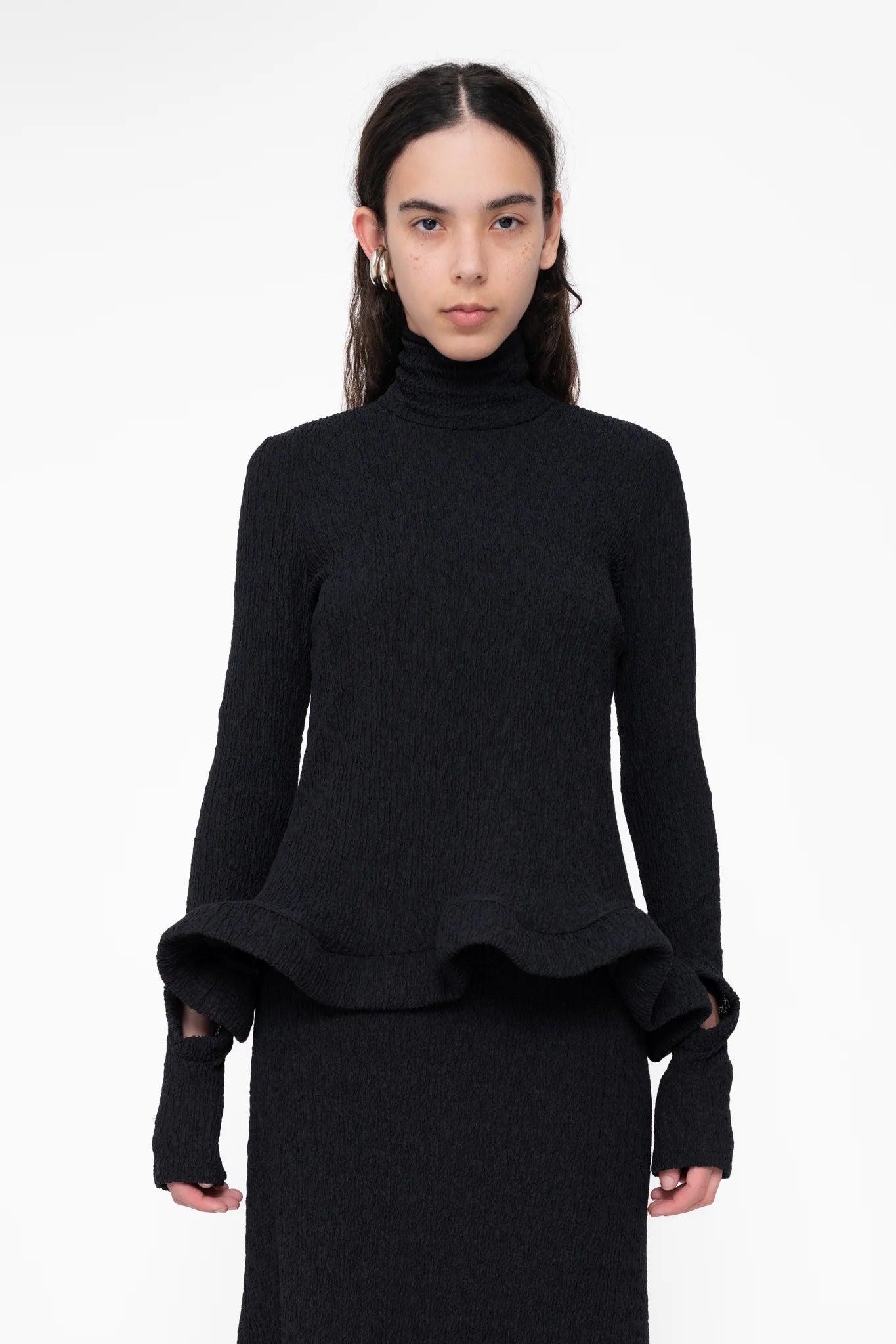 female-wearing-tight-black-longsleeve-turtleneck-top-with-wavy-hem-and-hole-in-sleeve-detail-on-white-background-ckose-up-torso-front