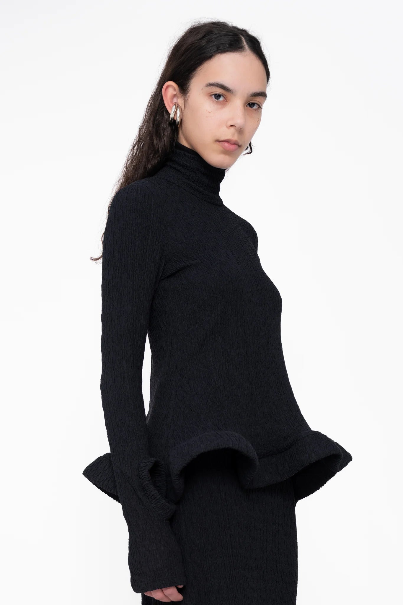 female-wearing-tight-black-longsleeve-turtleneck-top-with-wavy-hem-and-hole-in-sleeve-detail-on-white-background-ckose-up-torso-three-quarter