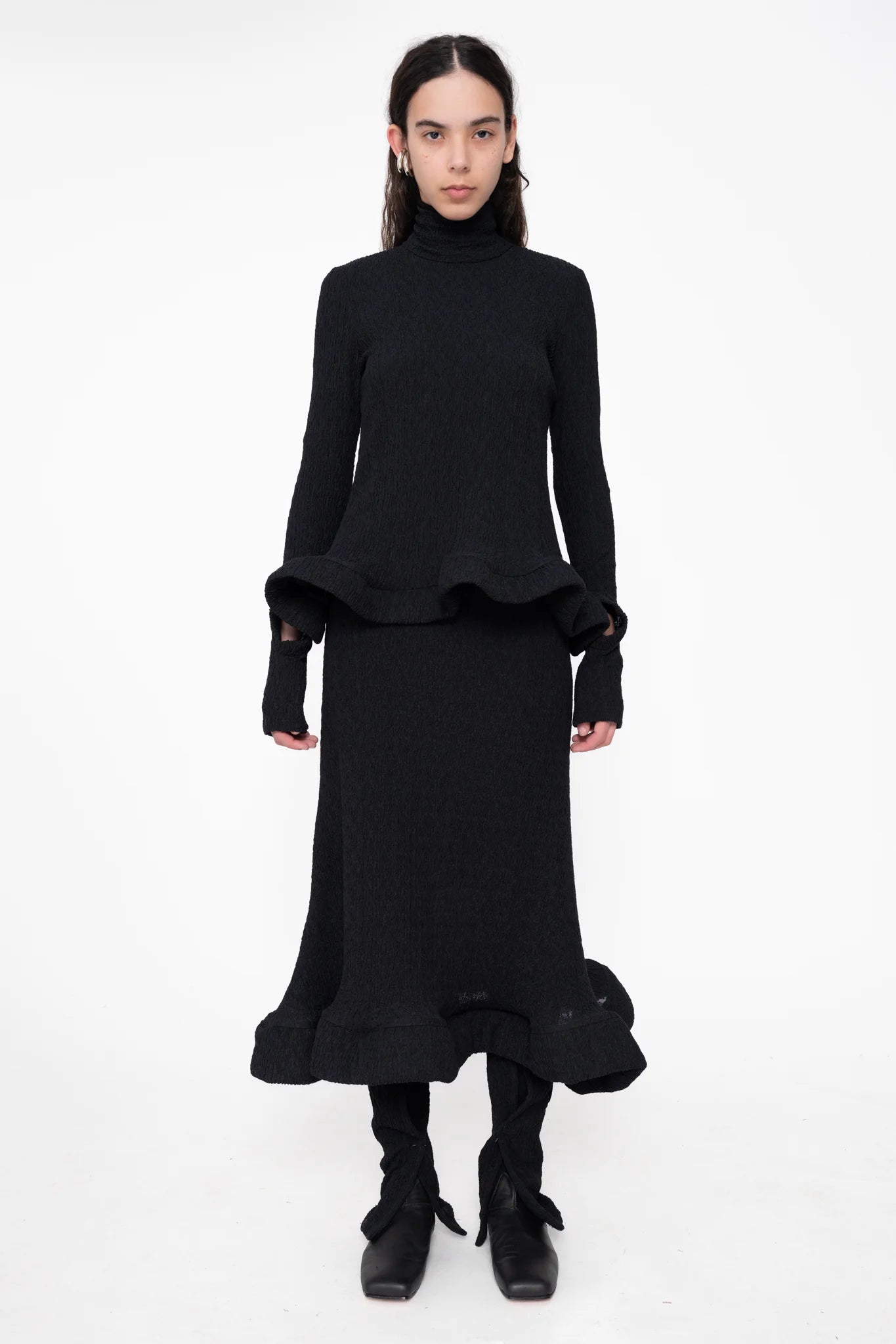 female-wearing-black-turtleneck-with-wavy-hem-and-matching-midi-skirt-on-white-background-full-body-front