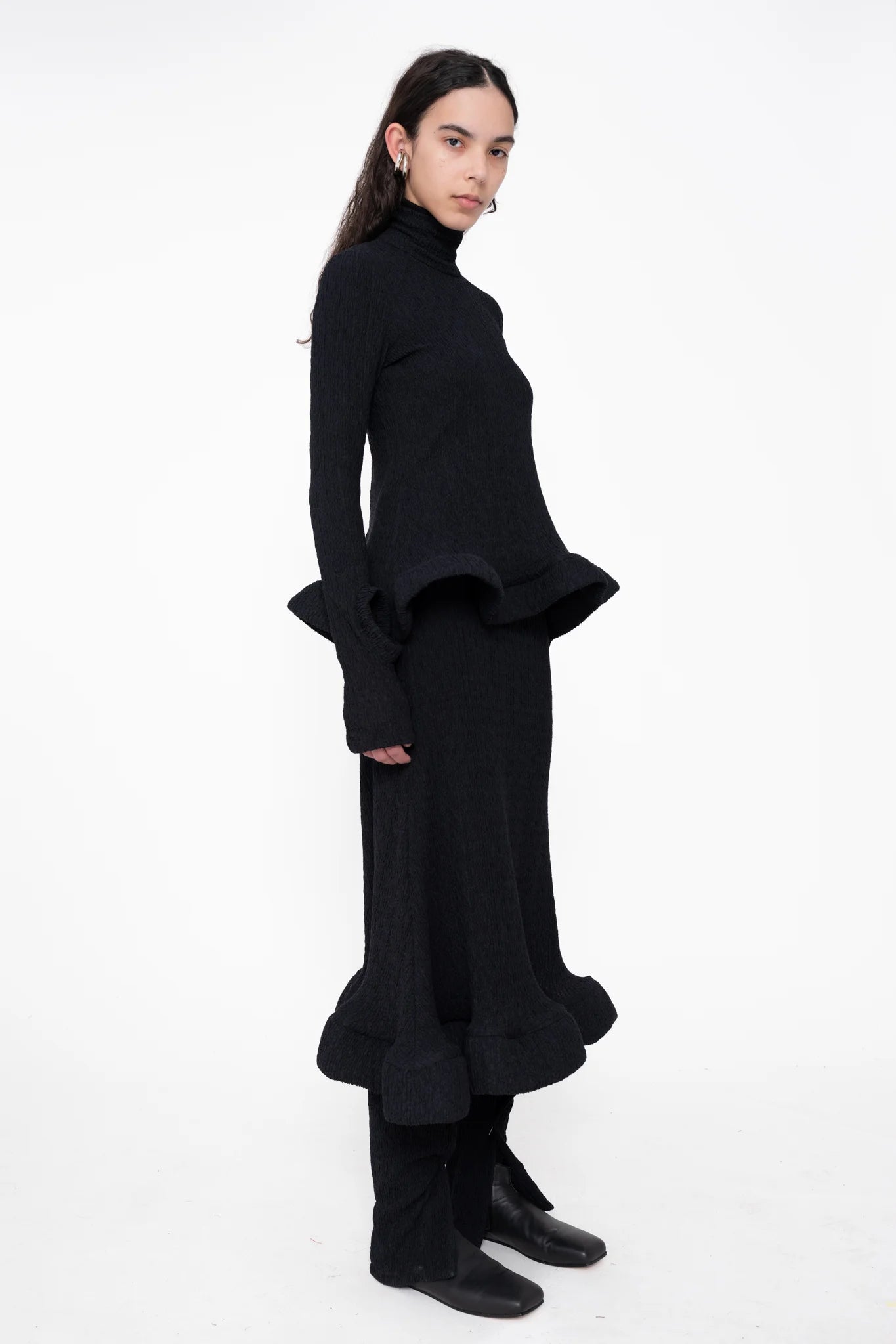 female-wearing-black-turtleneck-with-wavy-hem-and-matching-midi-skirt-on-white-background-full-body-three-quarter