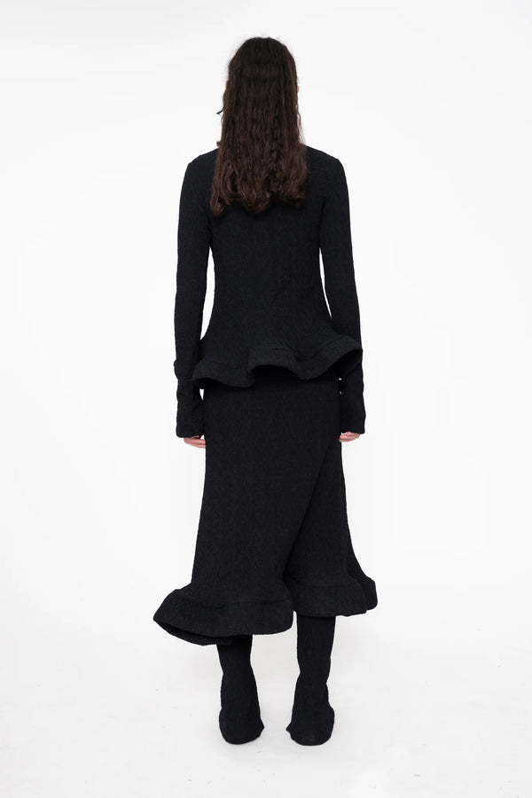 female-wearing-black-turtleneck-with-wavy-hem-and-matching-midi-skirt-on-white-background-full-body-back