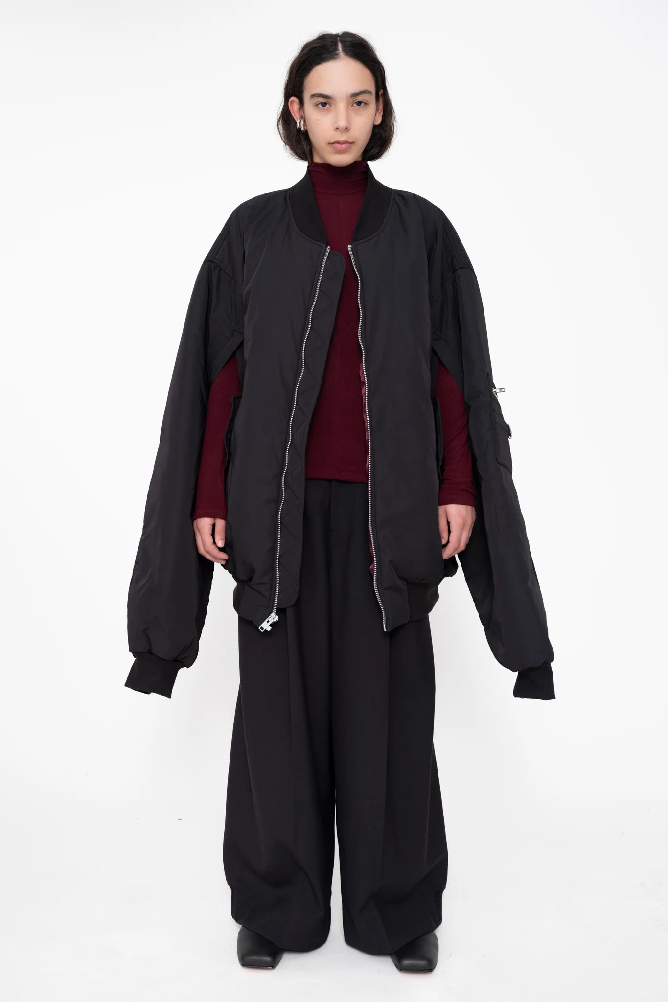 female-wearing-black-oversized-bomber-jacket-with-slits-paired-with-bordeaux-turtleneck-and-black-suit-pants-on-white-background-full-body-front