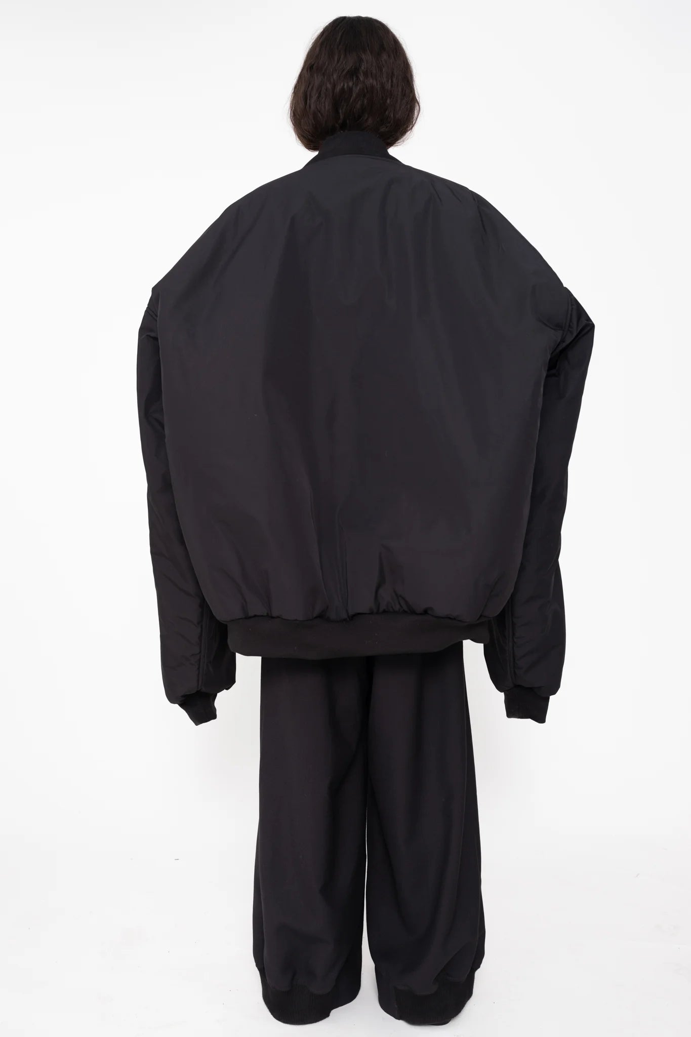 female-wearing-black-oversized-bomber-jacket-with-slits-paired-with-bordeaux-turtleneck-and-black-suit-pants-on-white-background-full-body-back