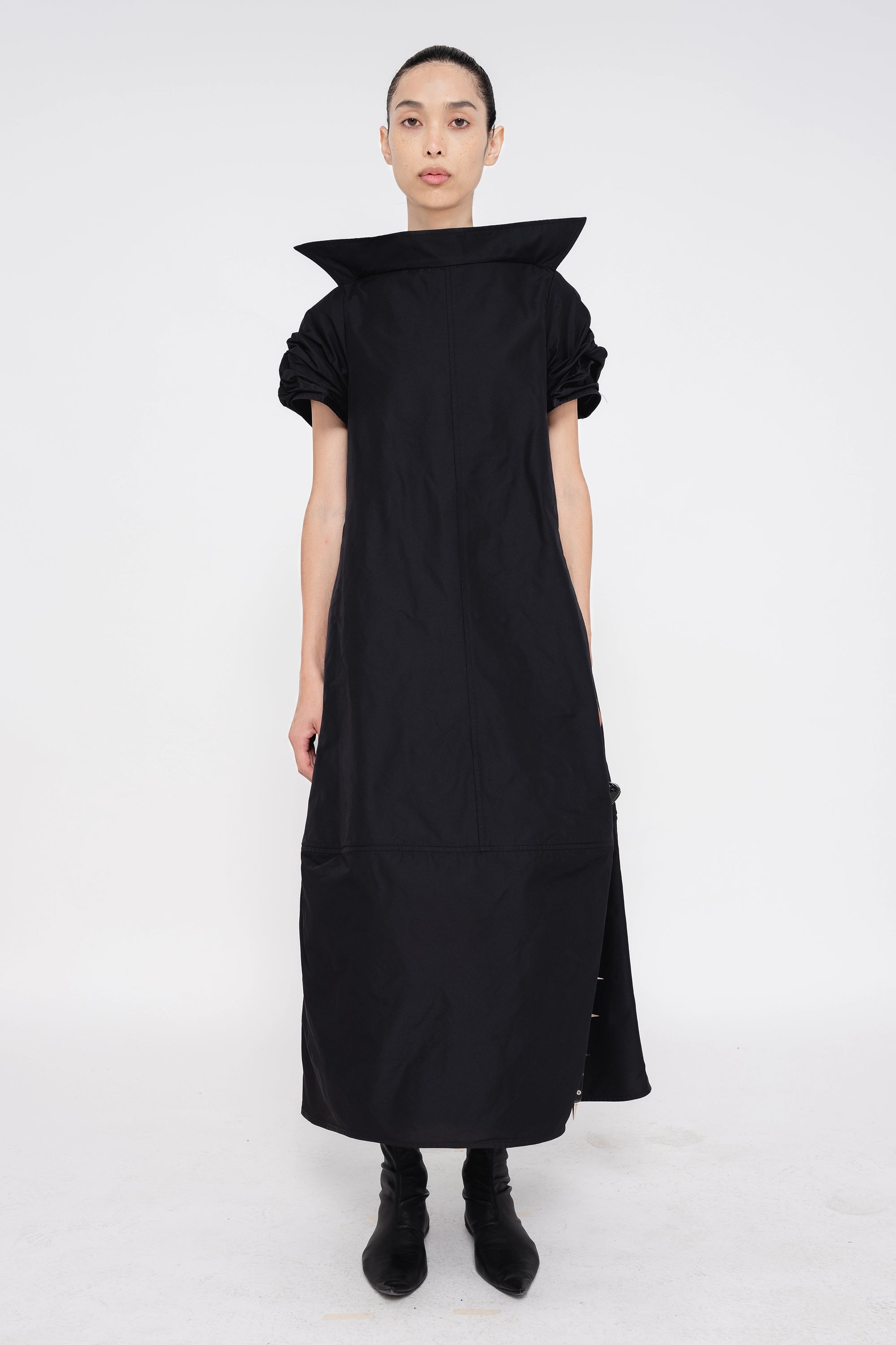 female-wearing-black-maxi-dress-with-stand-up-collar-and-short-pointy-sleeves-on-white-background-full-body-front