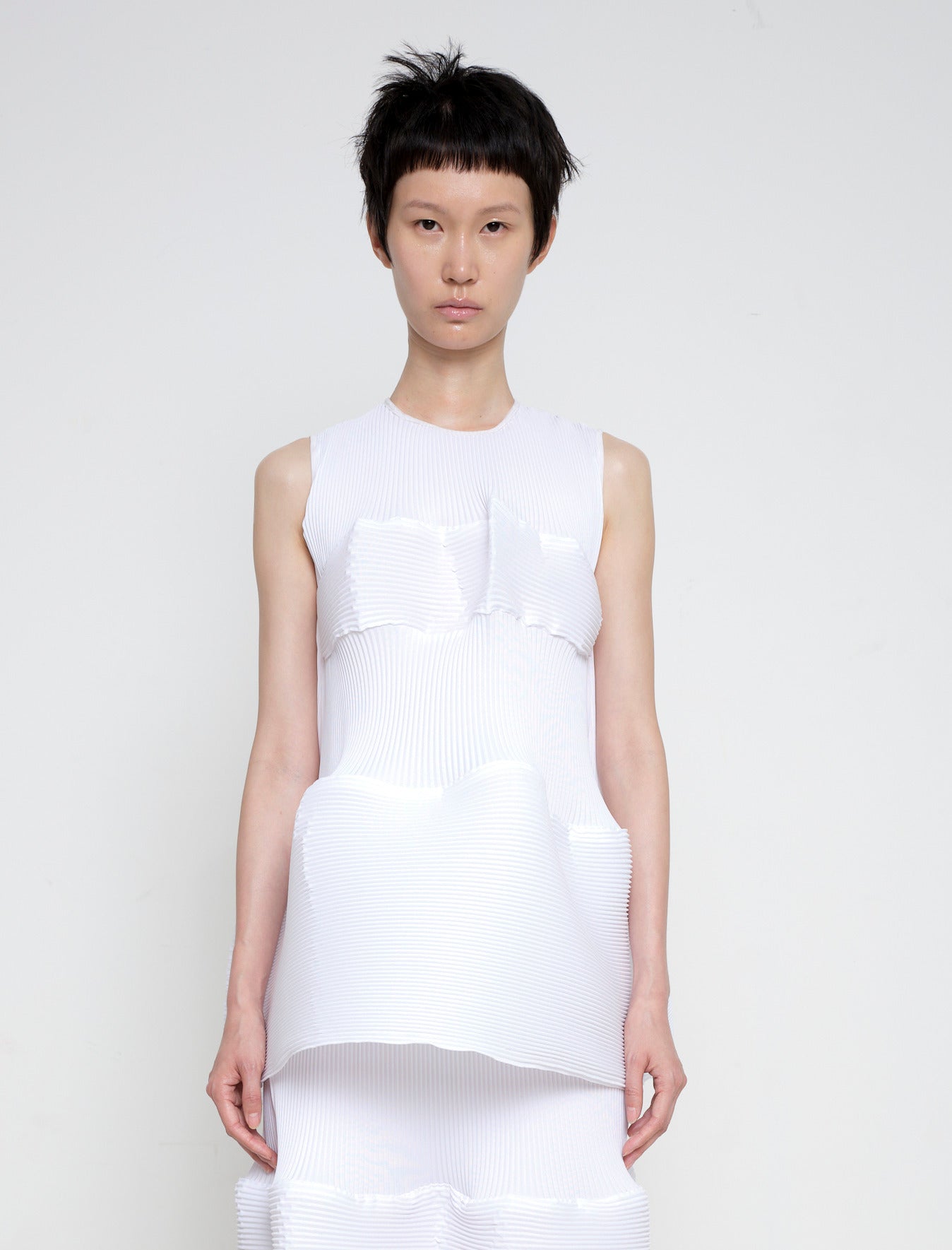 Woman-standing-against-white-background-wearing-Melitta-Baumeister's-white-sleeveless-ripple-top-with-fabric-design-at-the-chest-and-bottom