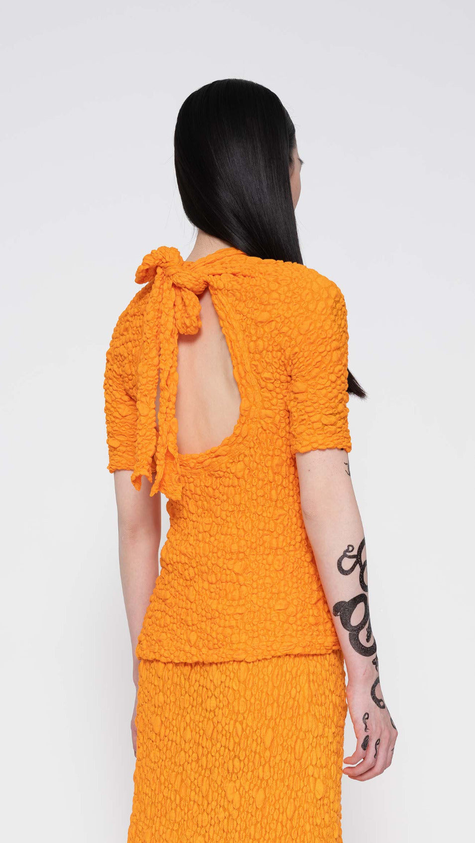 MELITTA-BAUMEISTER-Bow-Tie-Tee-Orange-Color-Long-Black-Hair-Female-Model-Back-View